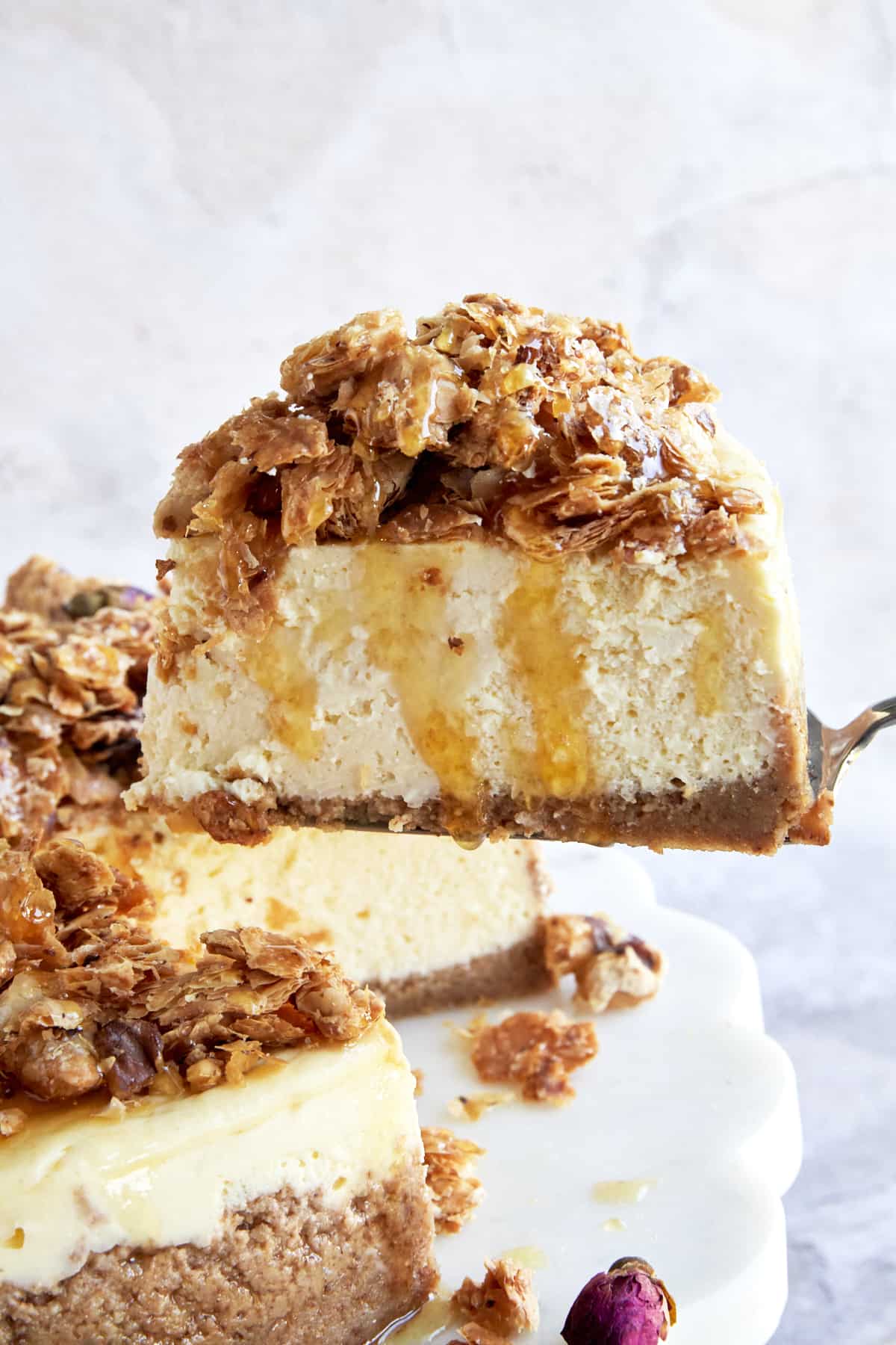 A slice of baklava cheesecake being lifted from a cake on a cake stand. 