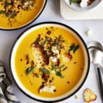 Two bowl of roasted butternut squash soup topped with feta crisps.