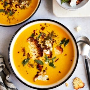 Two bowl of roasted butternut squash soup topped with feta crisps.