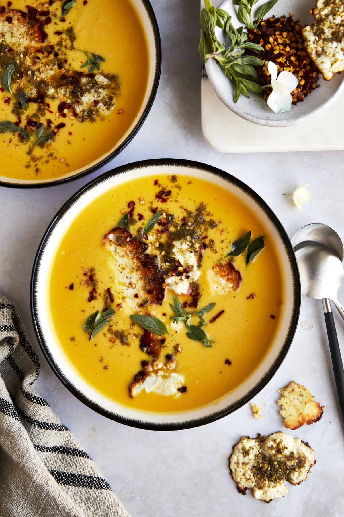 Two bowls of roasted butternut squash soup topped with feta crisps. 