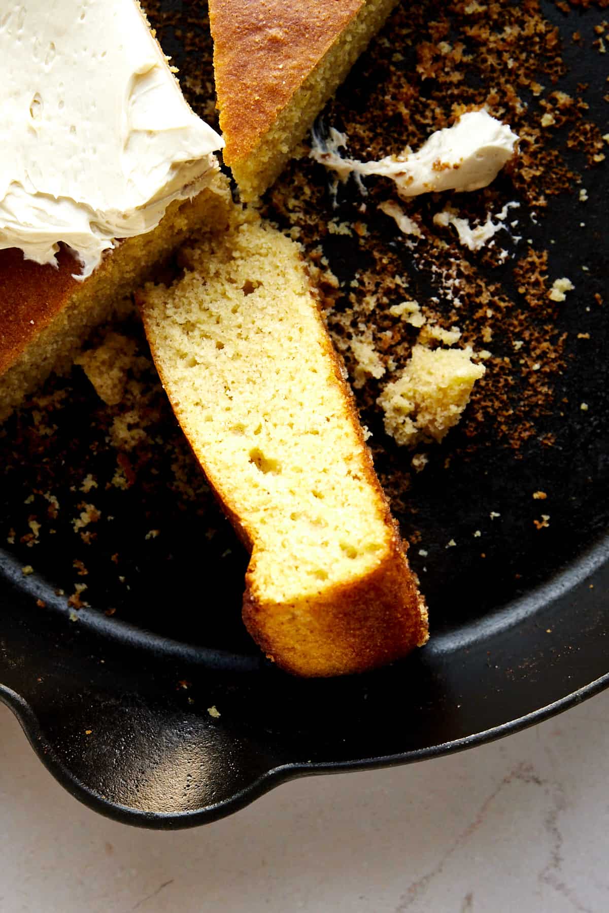 Pieces of brown butter cornbread in a a skillet topped with butter. 