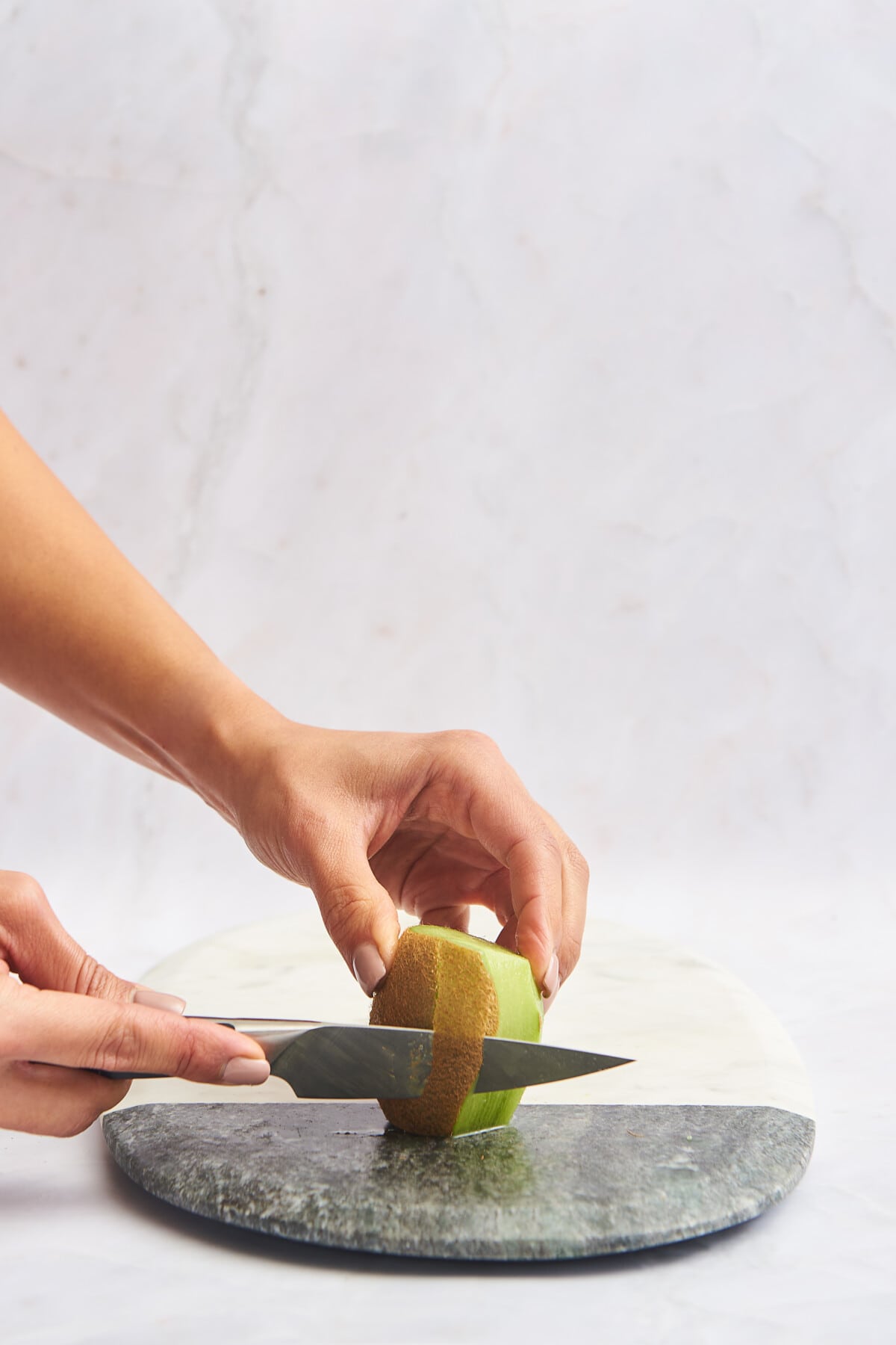 A knife being used to trim the skin off kiwi. 