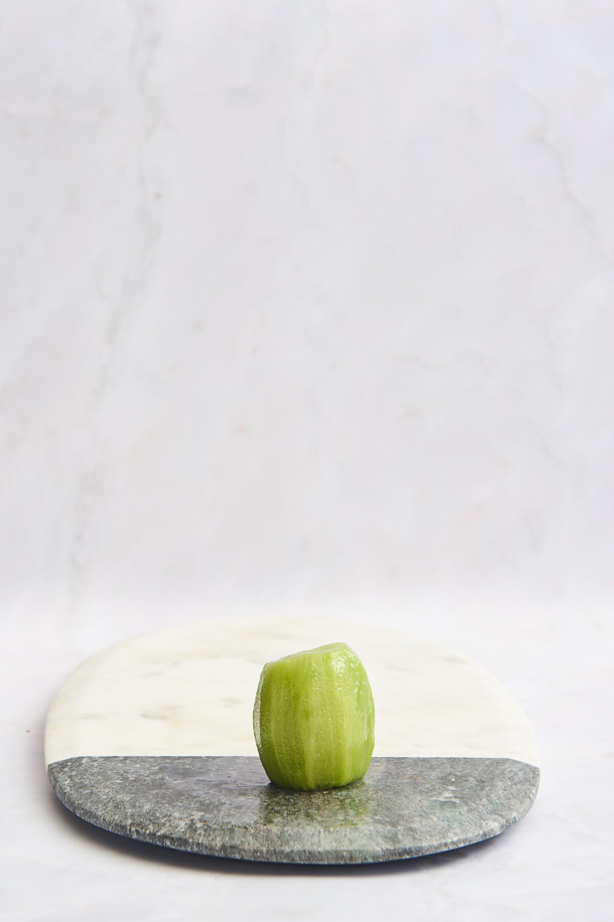 A kiwi without the skin on a cutting board. 