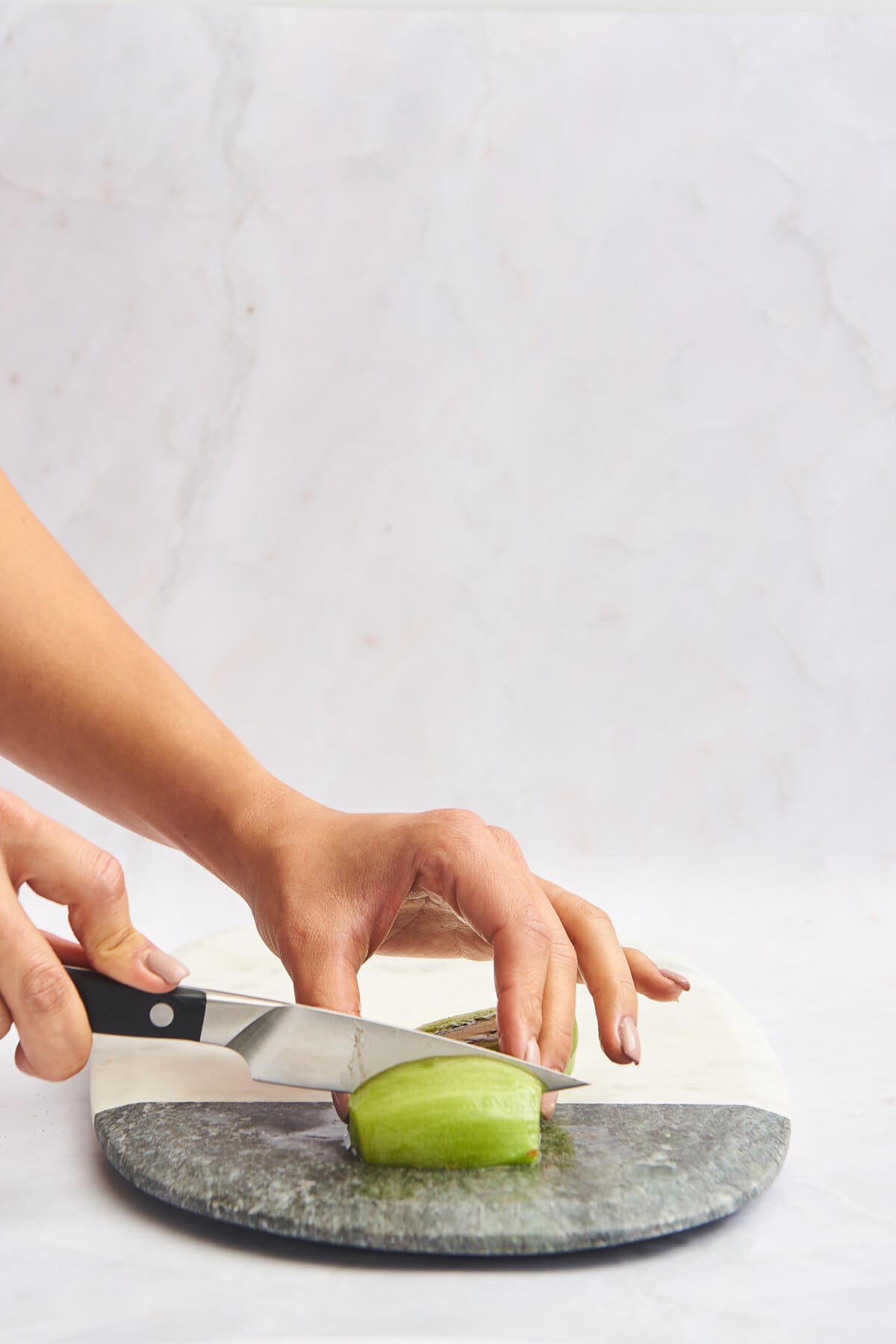 Hands cutting a skinless kiwi half into wedges. 