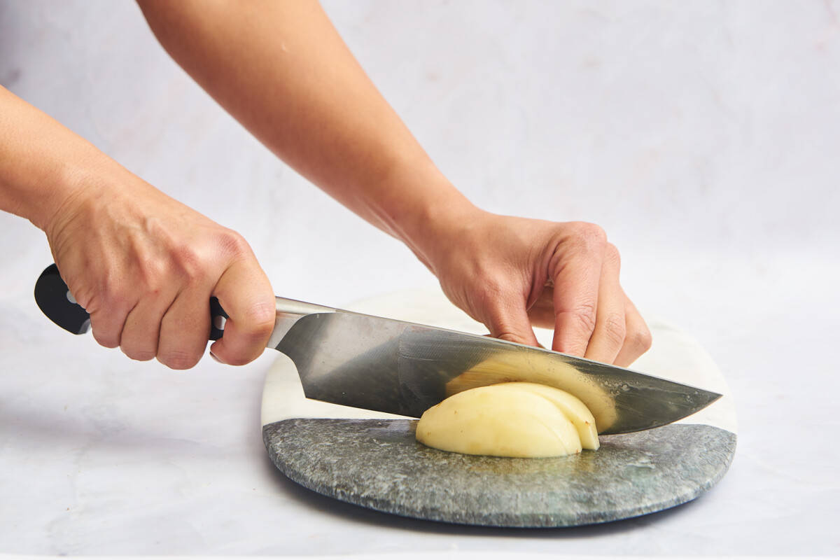 A peeled potato being cut into slices. 