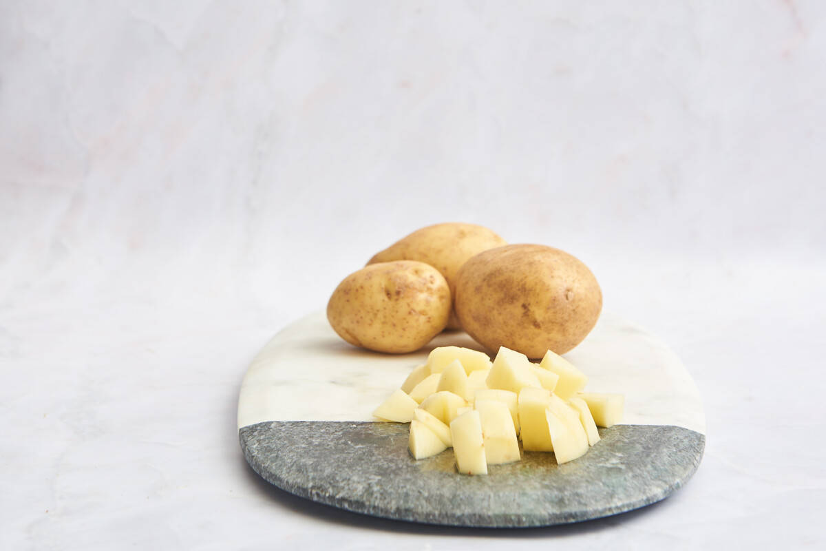 Whole potatoes and cubed potatoes on a cutting board. 