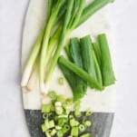 A cutting board with chopped green onions and halved green onions.