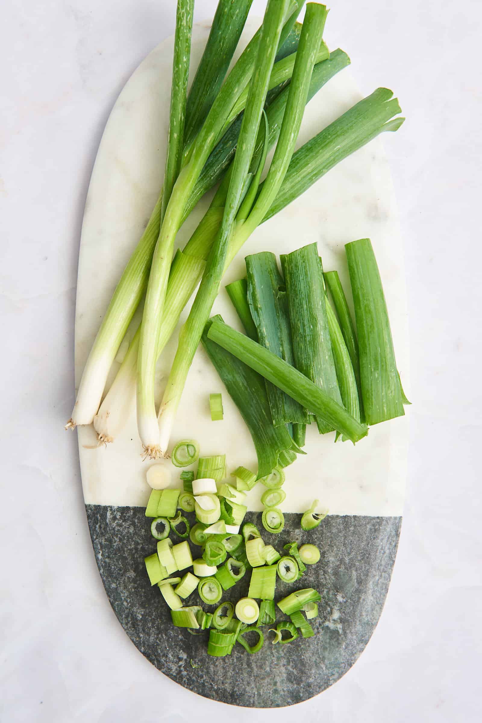 A cutting board with chopped green onions and halved green onions.