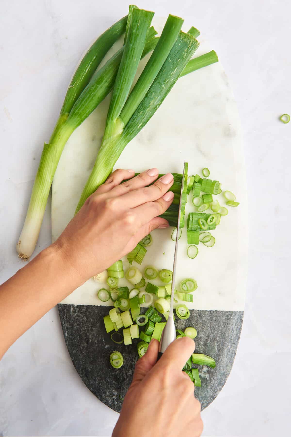 Green onions on a cutting board next to chopped green onions and a hand chopping scallions. 