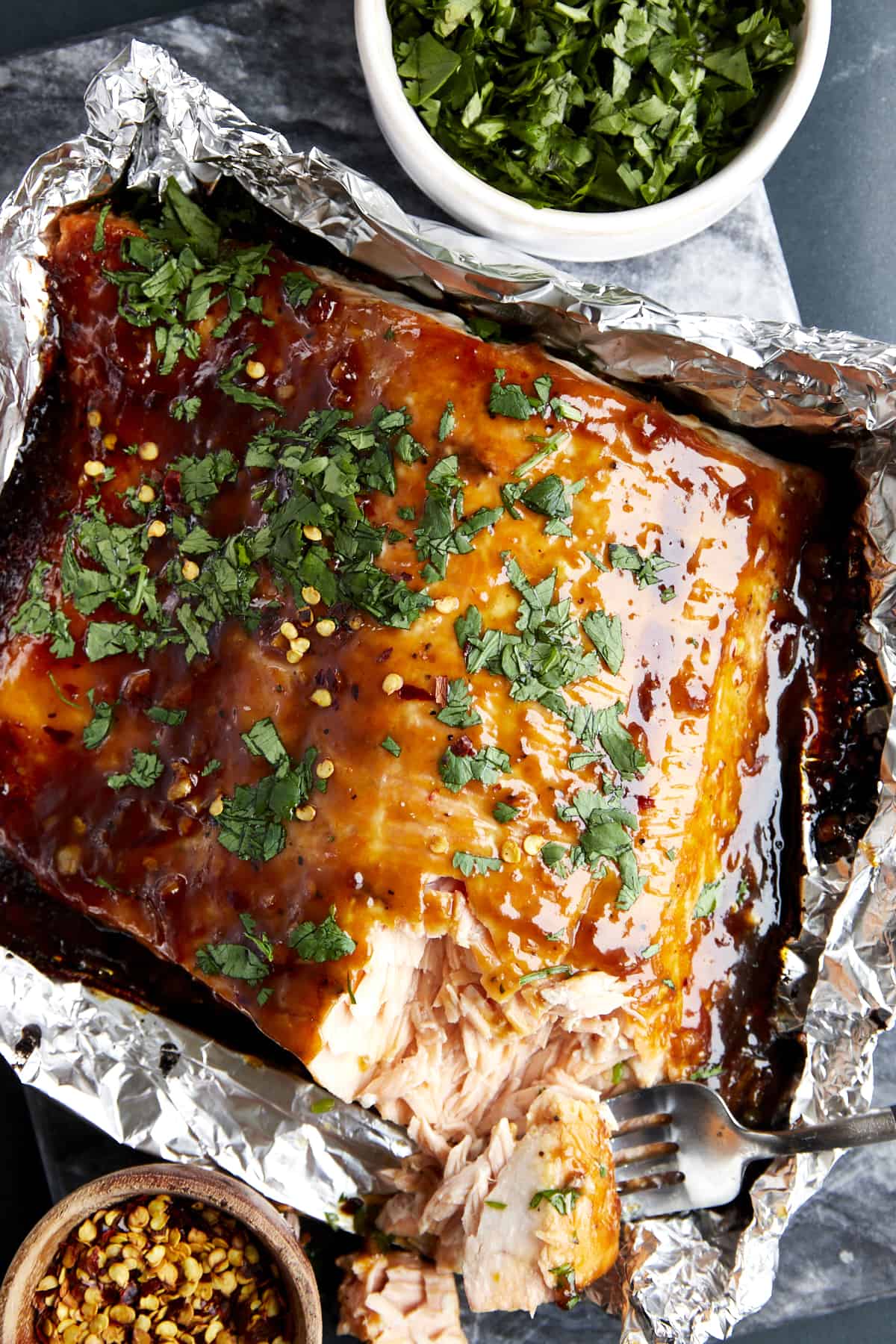 A fork taking a bite of honey garlic salmon in a foil packet. 