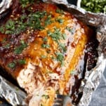 A fork tearing a bite of honey garlic salmon from a filet in a foil packet.