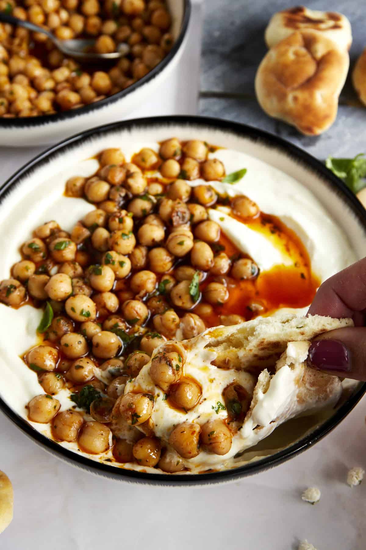 Pita bread being dipped into a bowl of whipped feta topped with marinated chickpeas. 