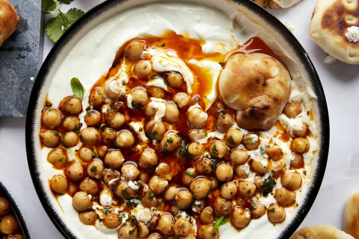 A bowl of whipped feta topped with marinated chickpeas with a piece of bread on top. 