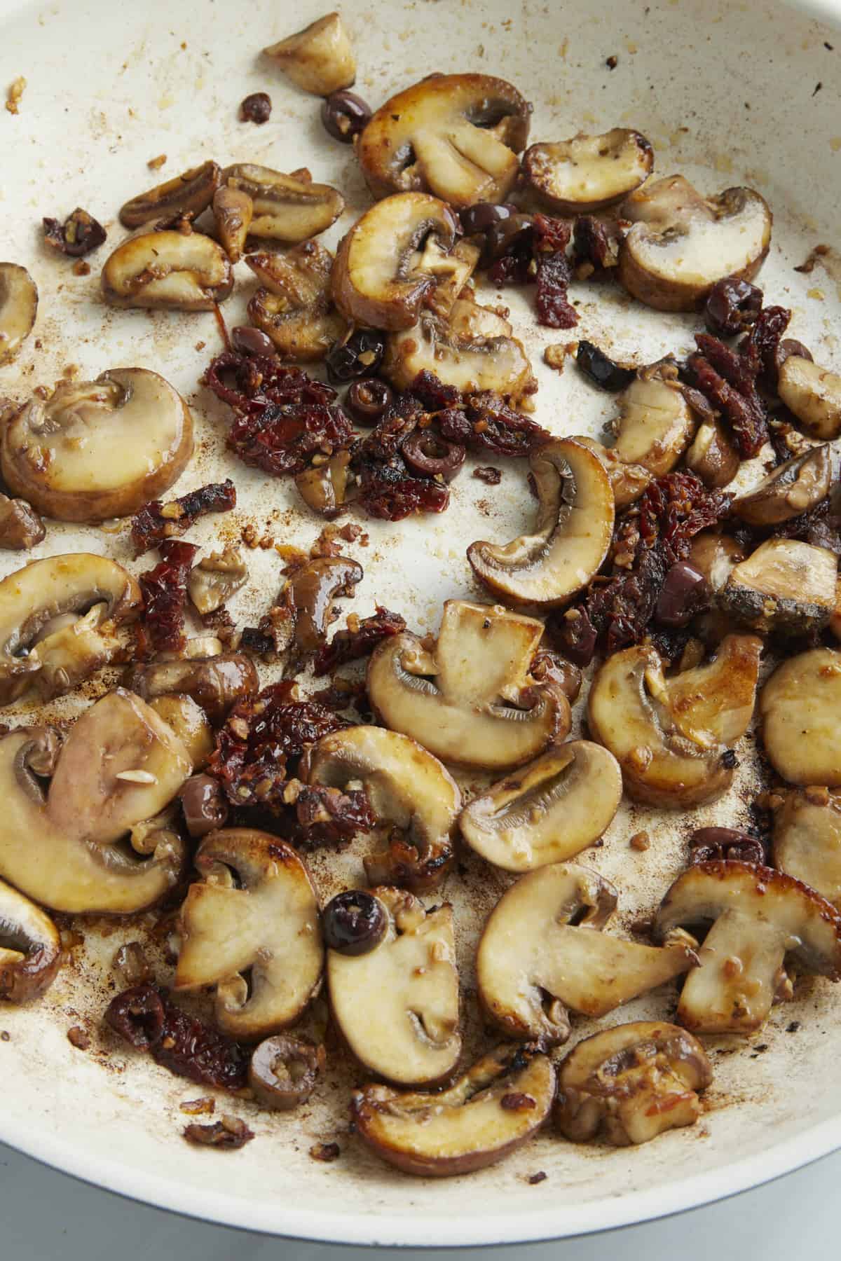 Mushrooms in a skillet with garlic and sun-dried tomatoes. 