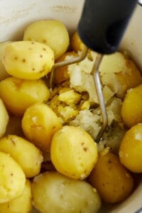 A potato masher mashing boiled potatoes.