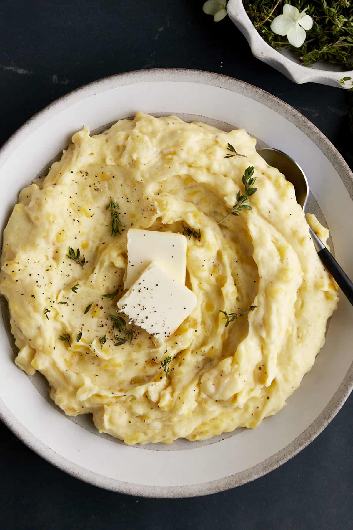 A bowl of mashed potatoes topped with black pepper, herbs, and butter. 