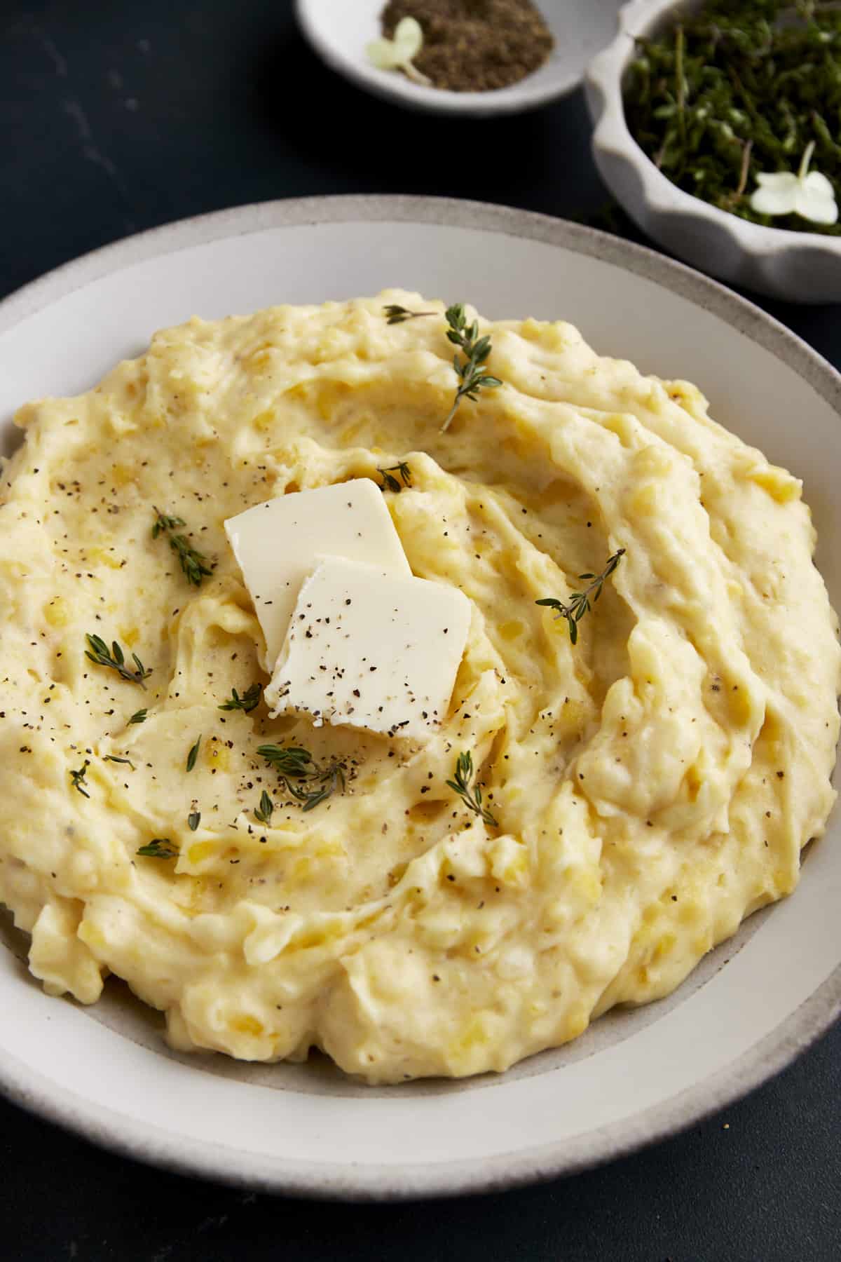 A bowl of the best mashed potatoes topped with butter, pepper, and herbs. 