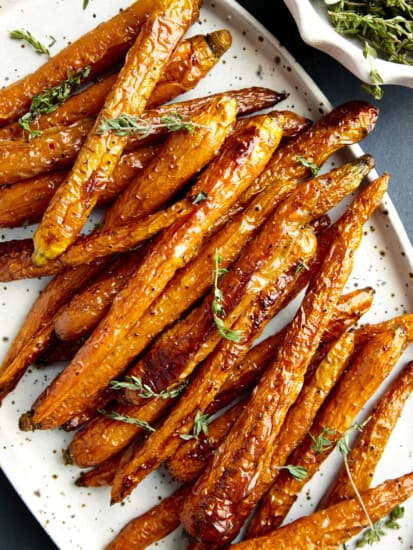 A platter of oven baked carrots topped with fresh herbs.