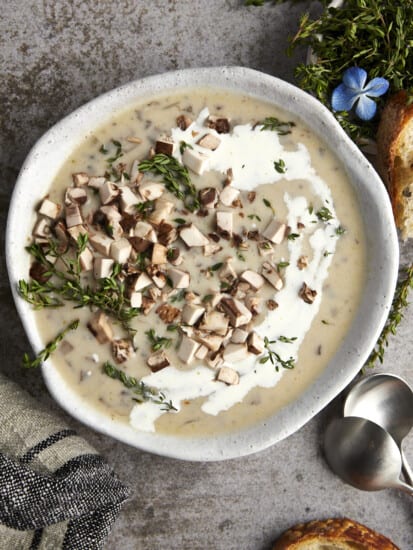 A bowl of creamy mushroom soup topped with mushrooms and thyme.