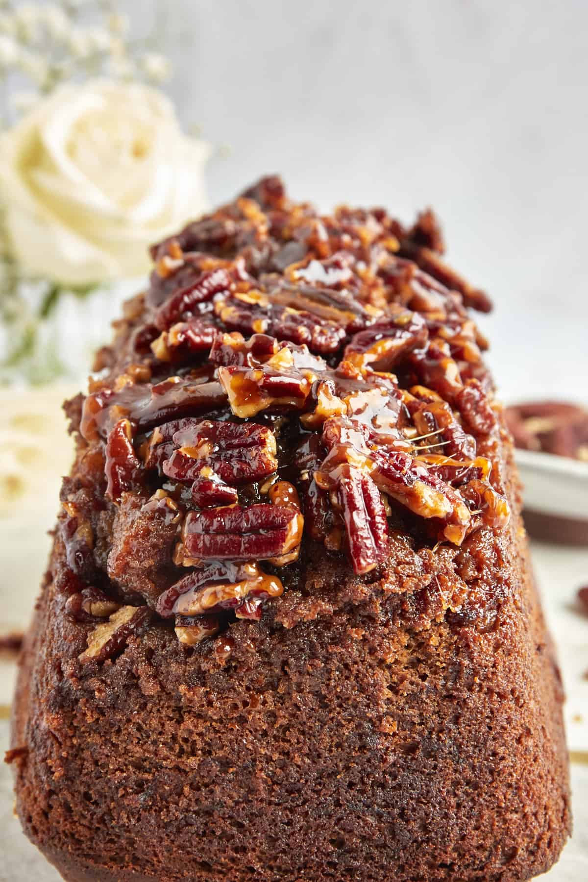 A loaf of banana pecan bread topped with a sticky pecan topping. 