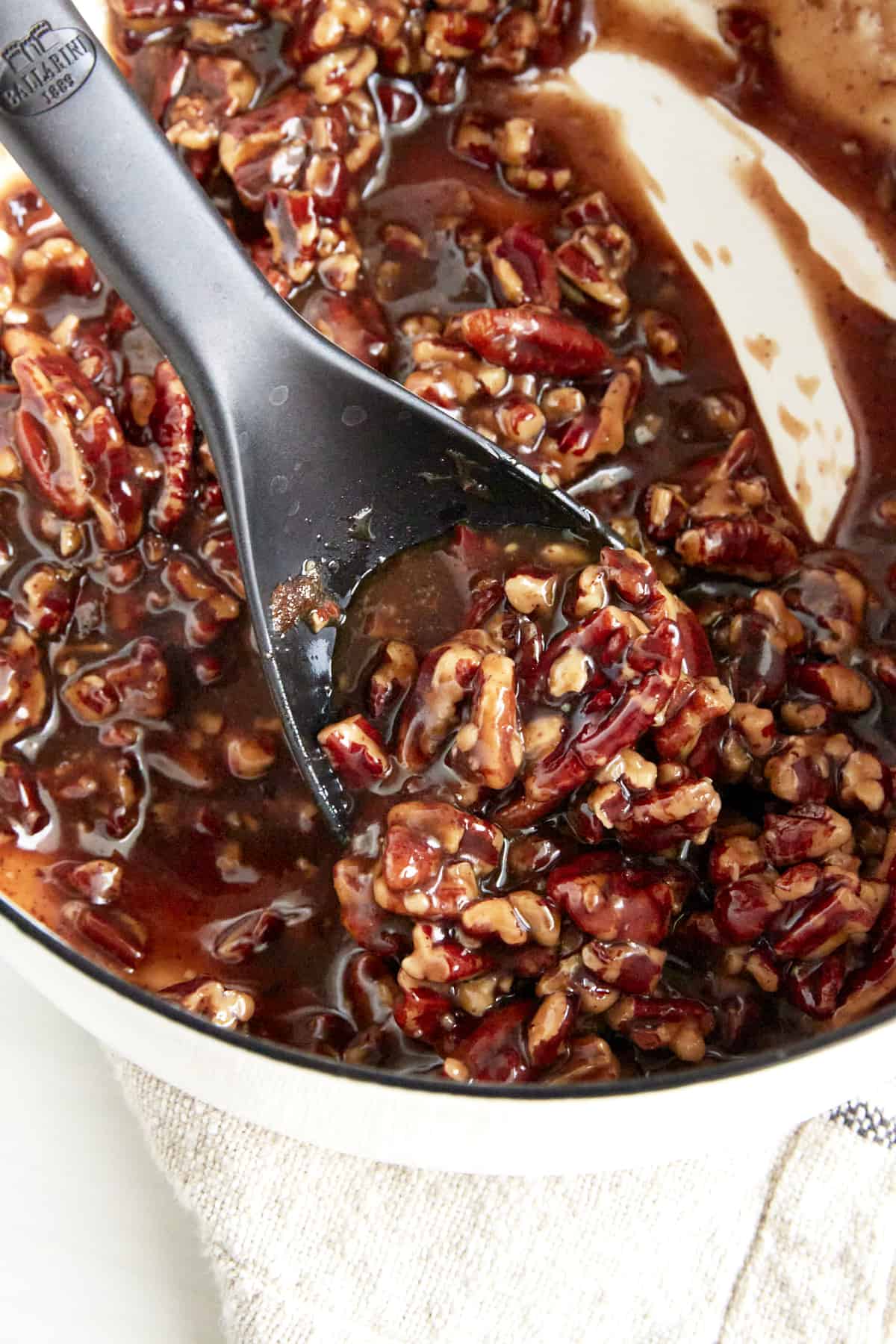 Pecan pie filling in a saucepan being stirred with a spoon. 