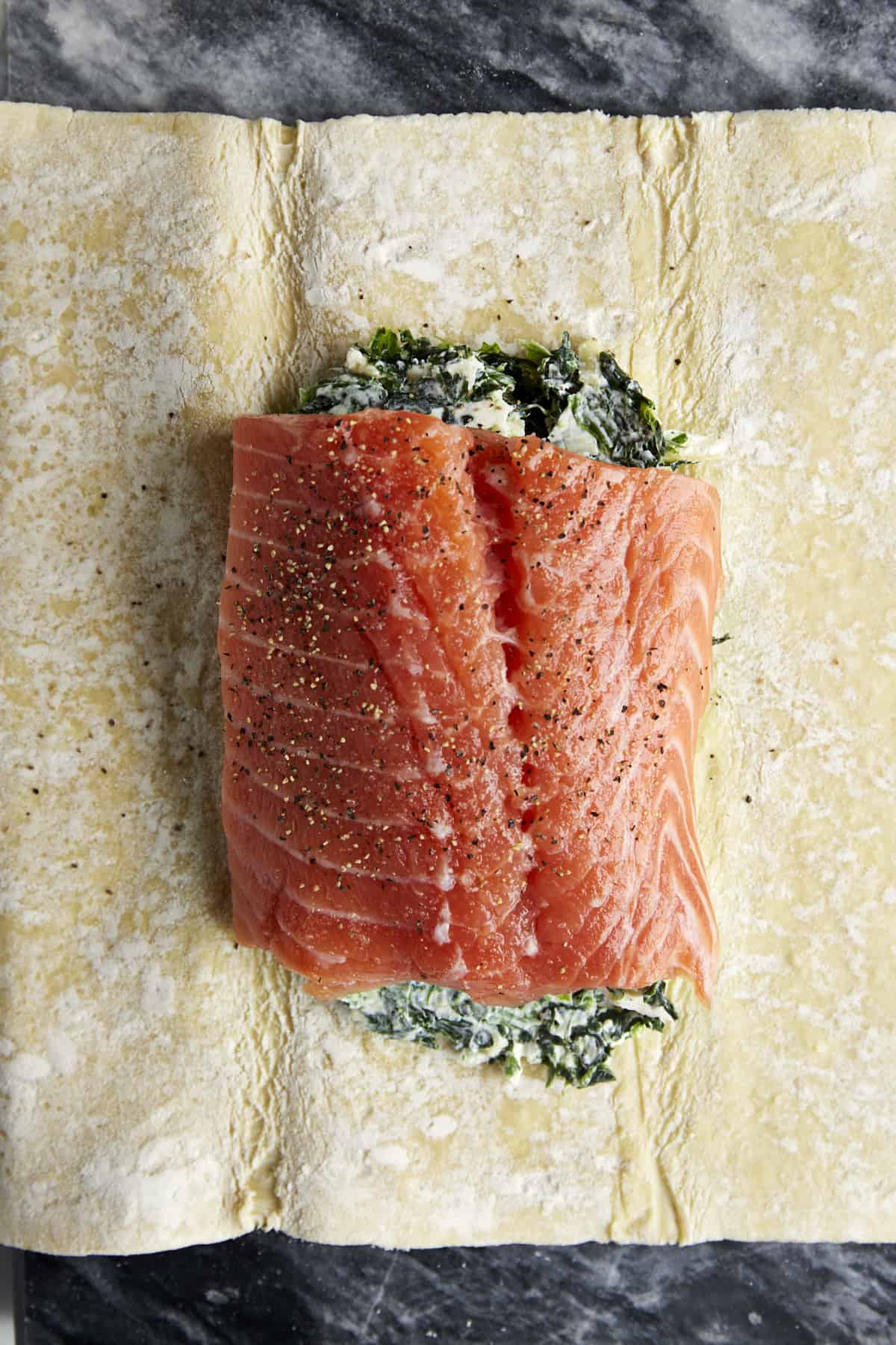 Puff pastry topped with a cheese and spinach mixture and a raw salmon filet.