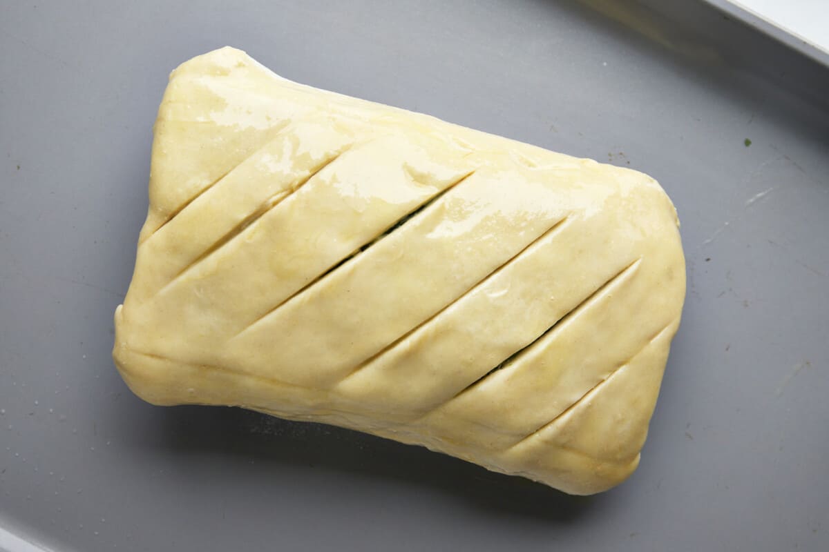Unbaked Salmon Wellington with slits in the top of the dough. 