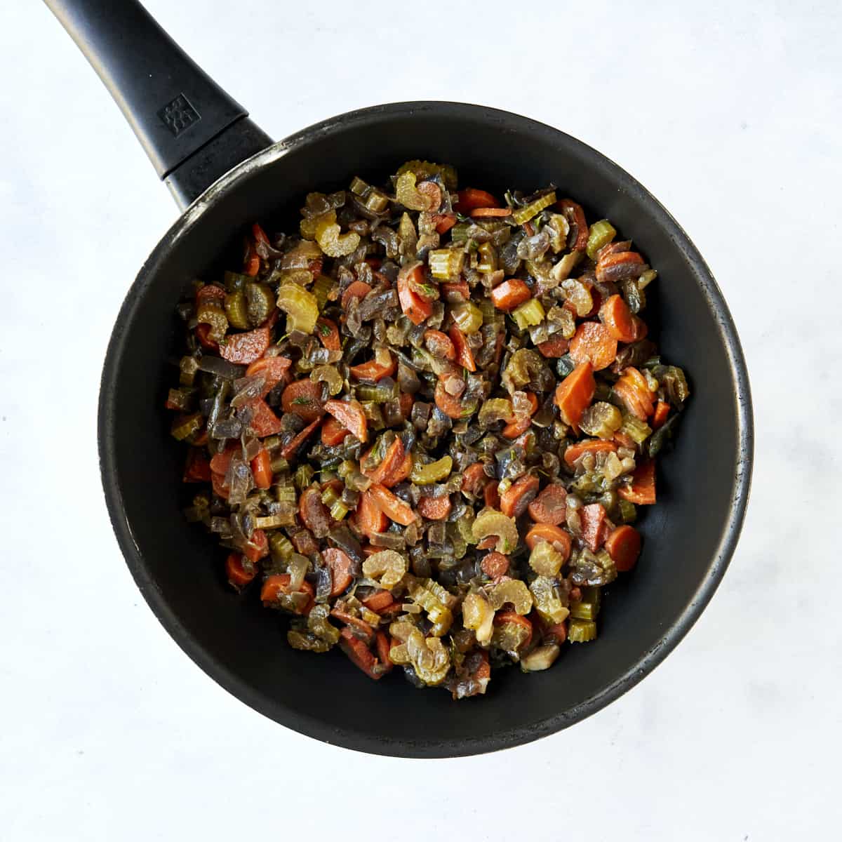 Sautéed veggies in a skillet and a mixing bowl full of Mediterranean-style dressing ingredients. 