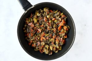 Sautéed veggies, seasonings, and olives in a skillet.