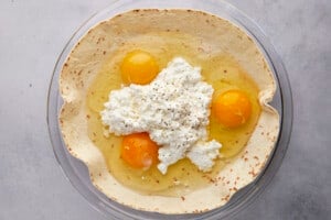 Raw eggs and cottage cheese over a tortilla in a dish.