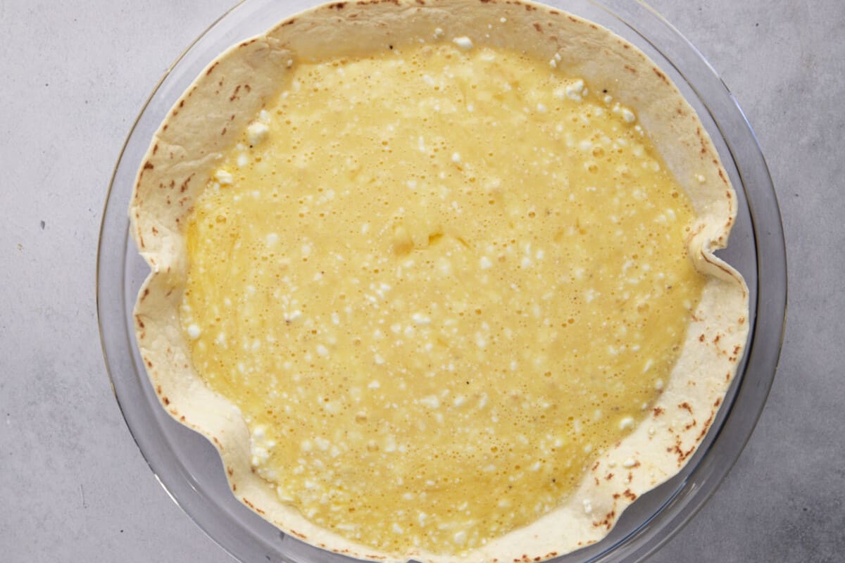 An unbaked egg and cottage cheese mixture over a tortilla in a round dish. 