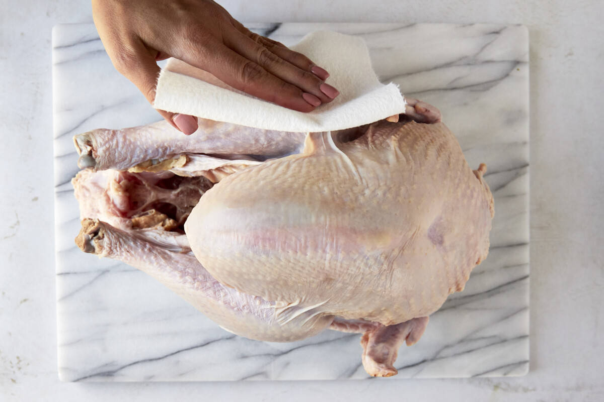 A raw turkey being pat dry. 