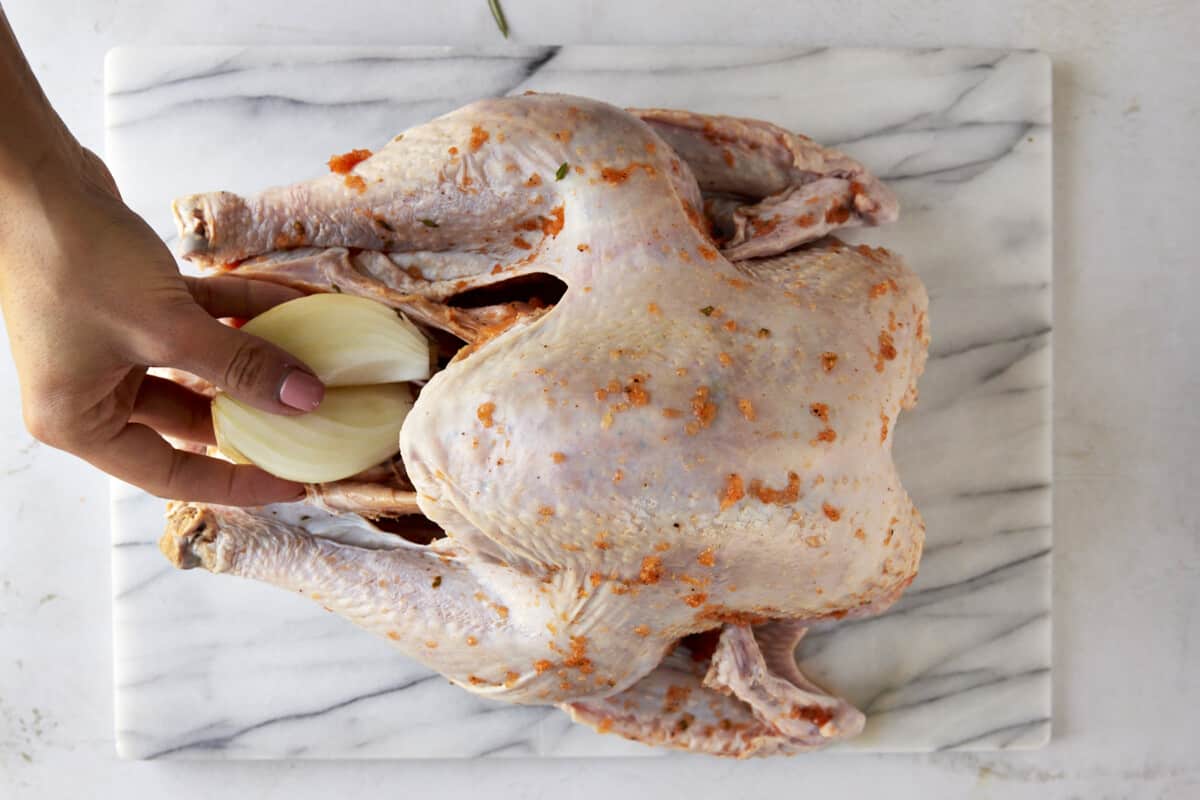 An onion halve being placed in a turkey cavity. 