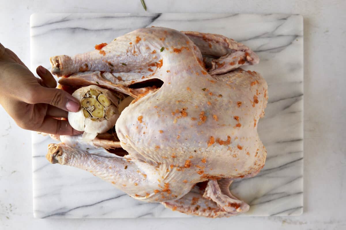 A garlic head being placed in a turkey cavity. 