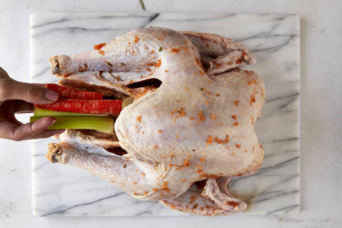 Celery and carrot sticks being placed inside a turkey. 