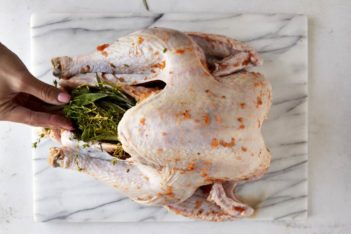 Herbs being placed inside a raw turkey. 