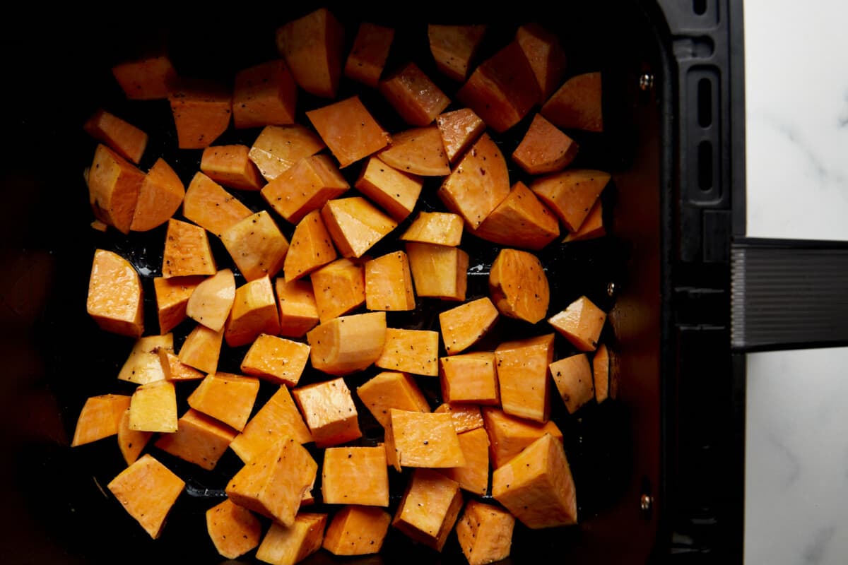 Raw sweet potato cubes in an air fryer basket. 