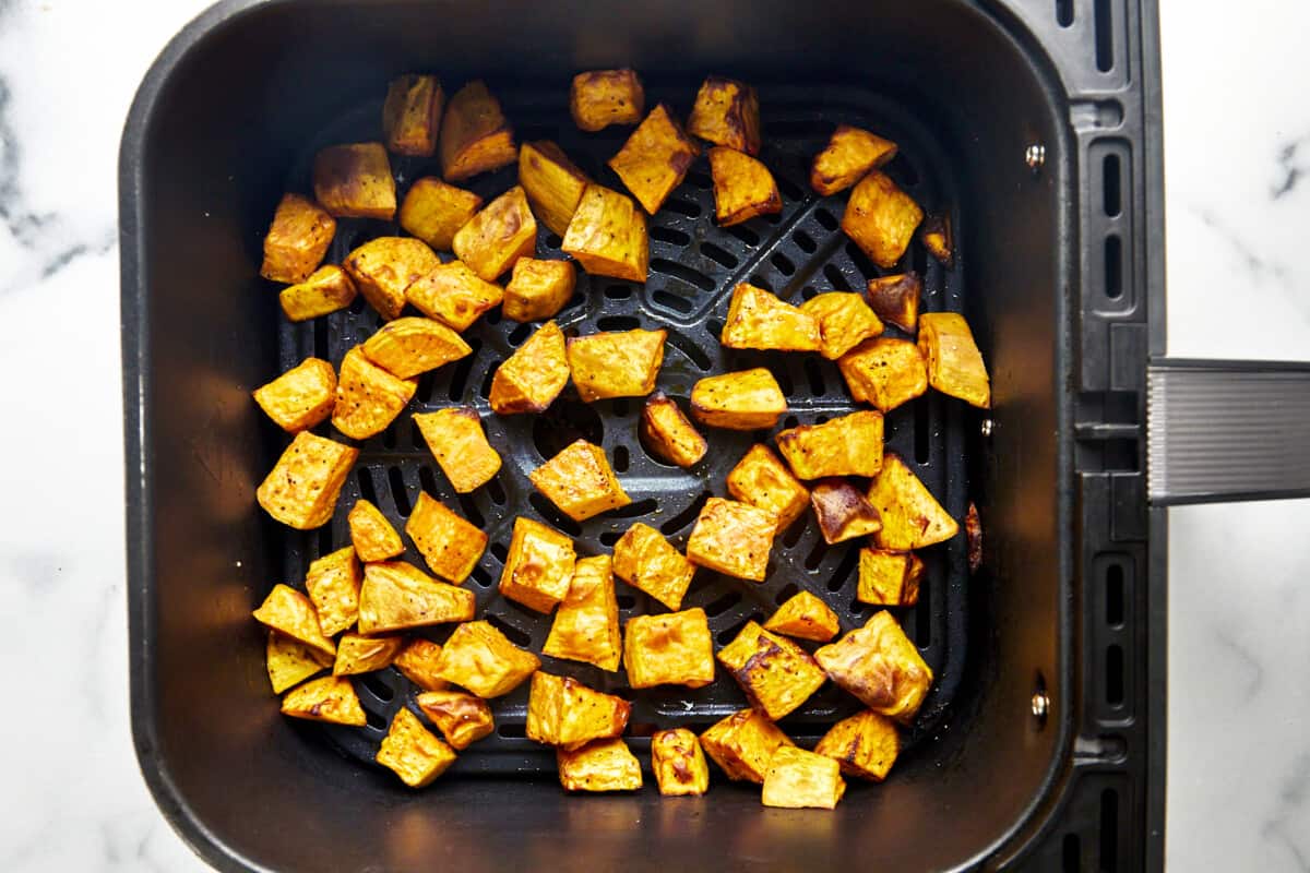 Cooked sweet potato cubes in an air fryer basket. 