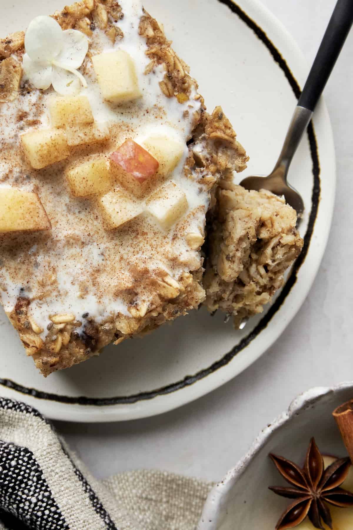 Baked apple oatmeal on a plate topped with apples and milk with a fork holding a bite. 