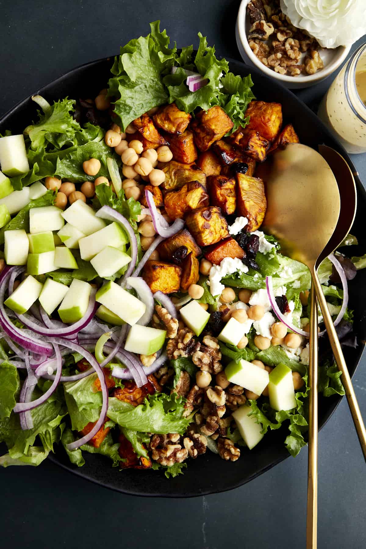 Close view of an undressed sweet potato salad with chickpeas in a bowl with golden serving spoons. 