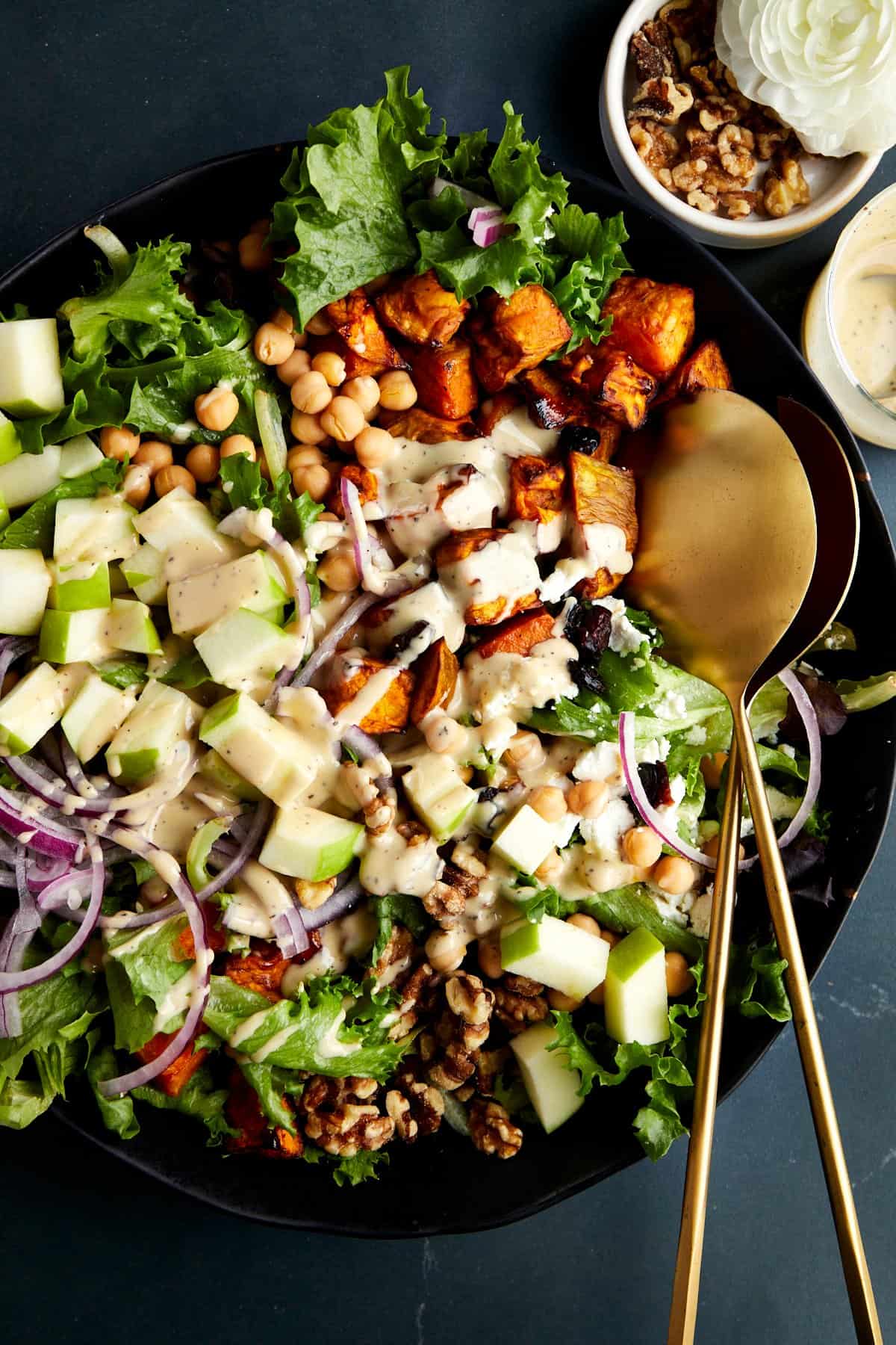 A bowl of sweet potato salad topped with tahini dressing with serving spoons on the side. 