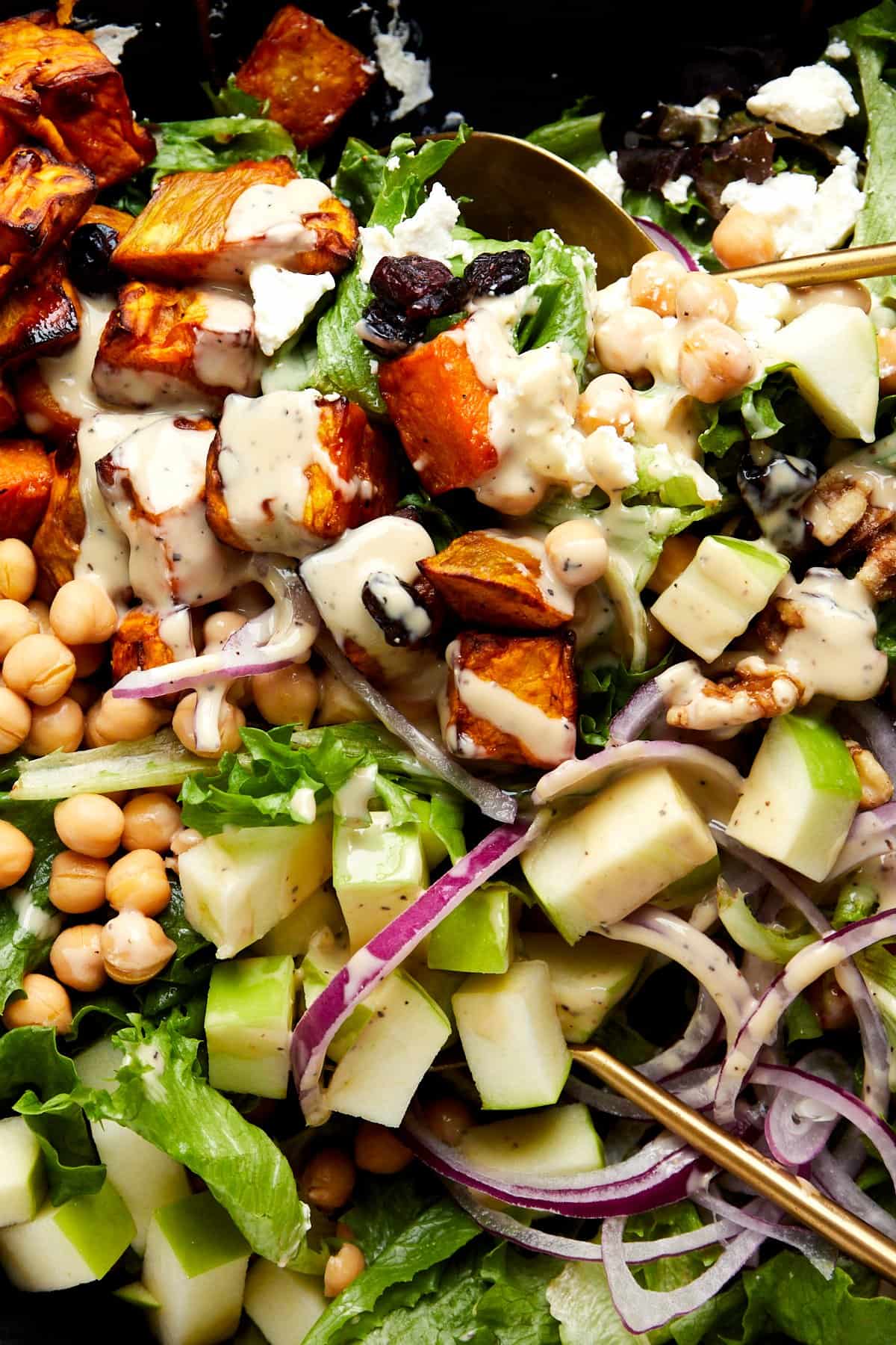 A gold serving spoon sinking into a bowl of sweet potato salad dressed with tahini dressing.