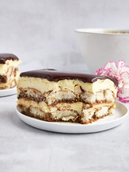 A slice of tiramisu eclair cake on a plate with a bite missing from the corner.