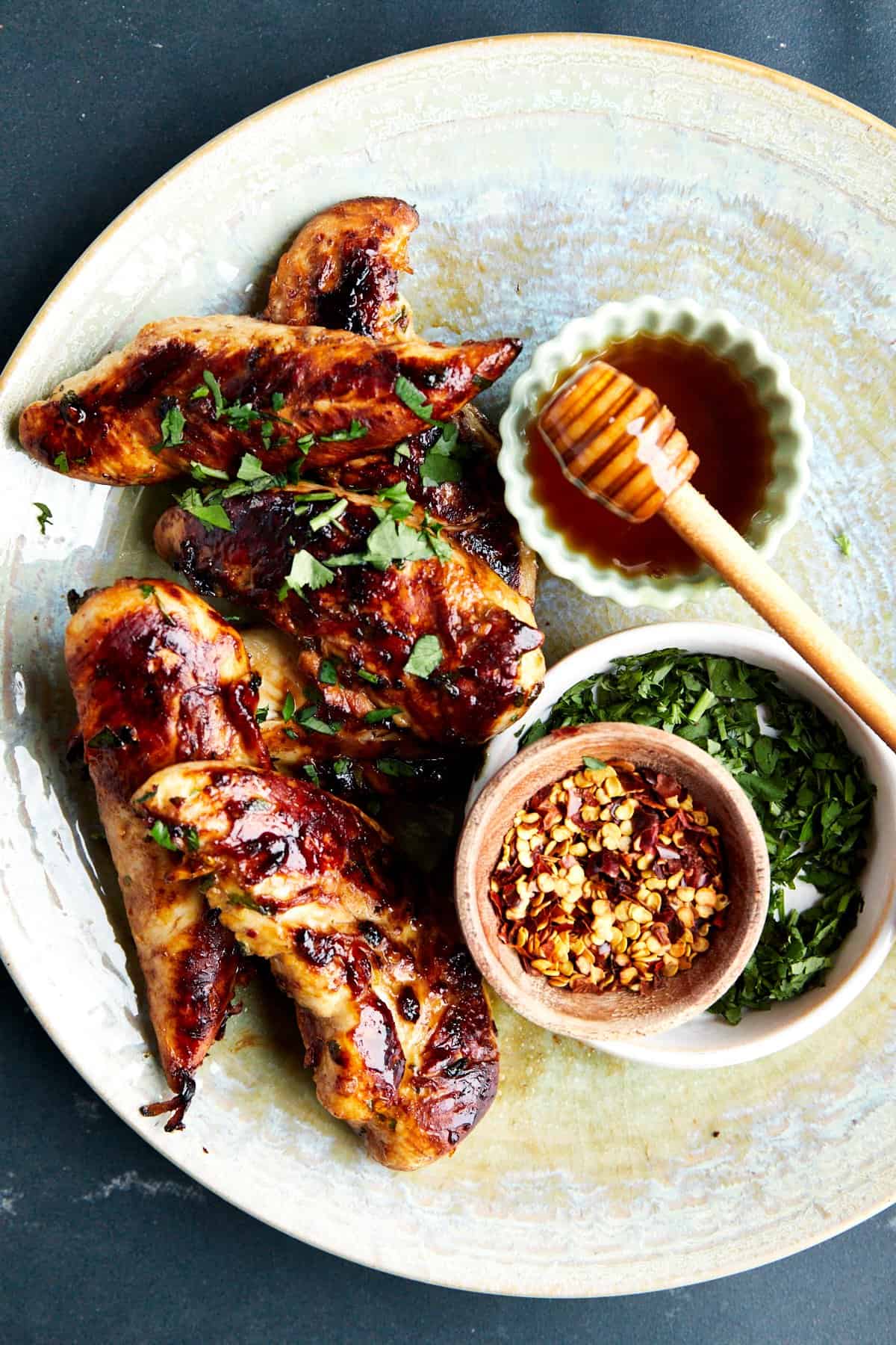 A bowl of honey garlic chicken tenders with honey, chili flakes, and green onions. 