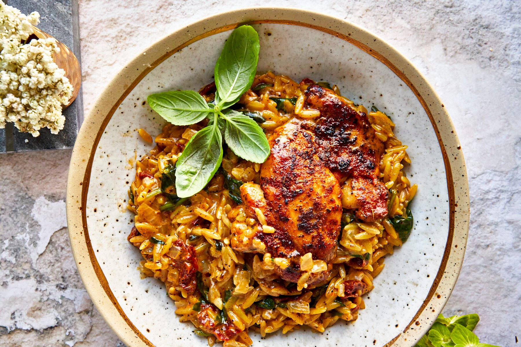 A bowl of chicken and orzo topped with parsley.