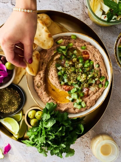 A hand dipping a pita chip into a bowl of ful medames.