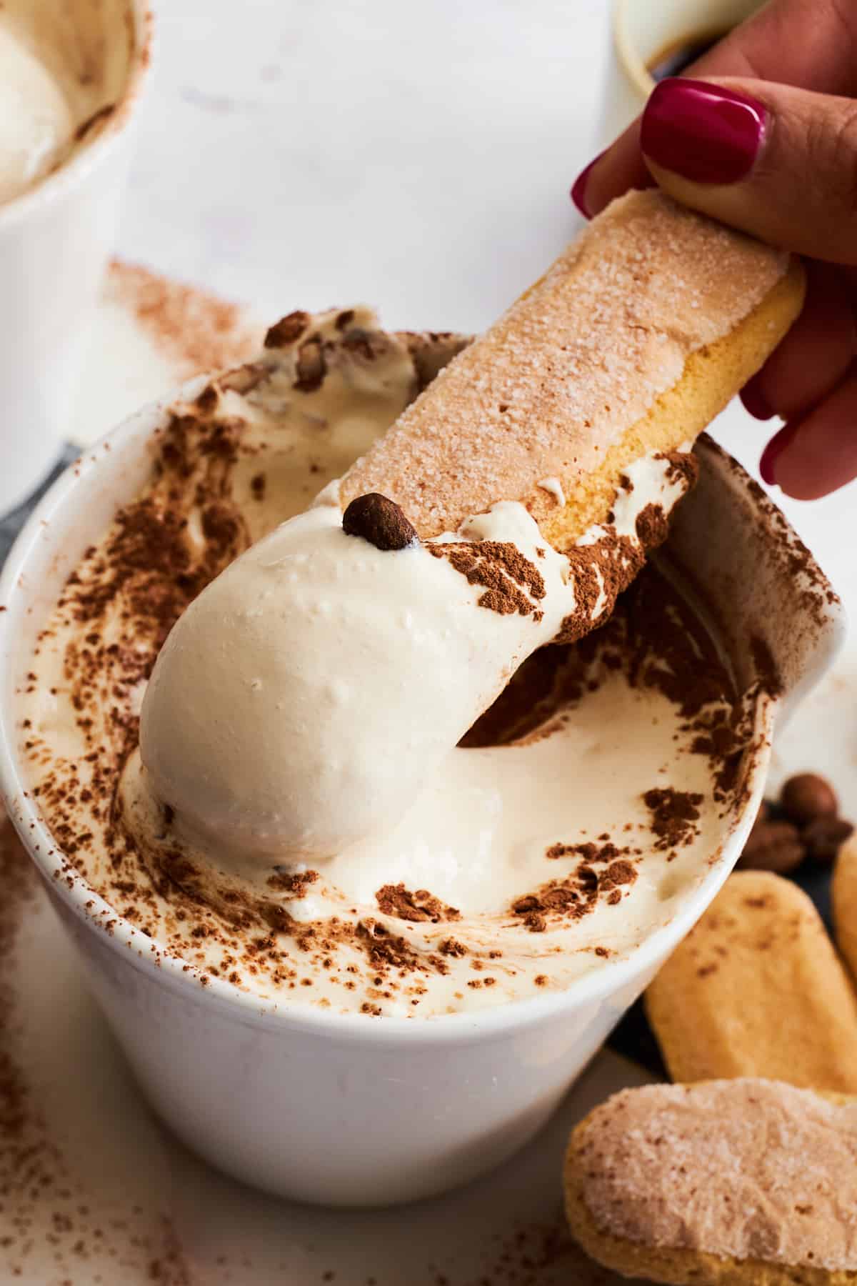 A ladyfinger cookie being dipped into a bowl of tiramisu dip. 