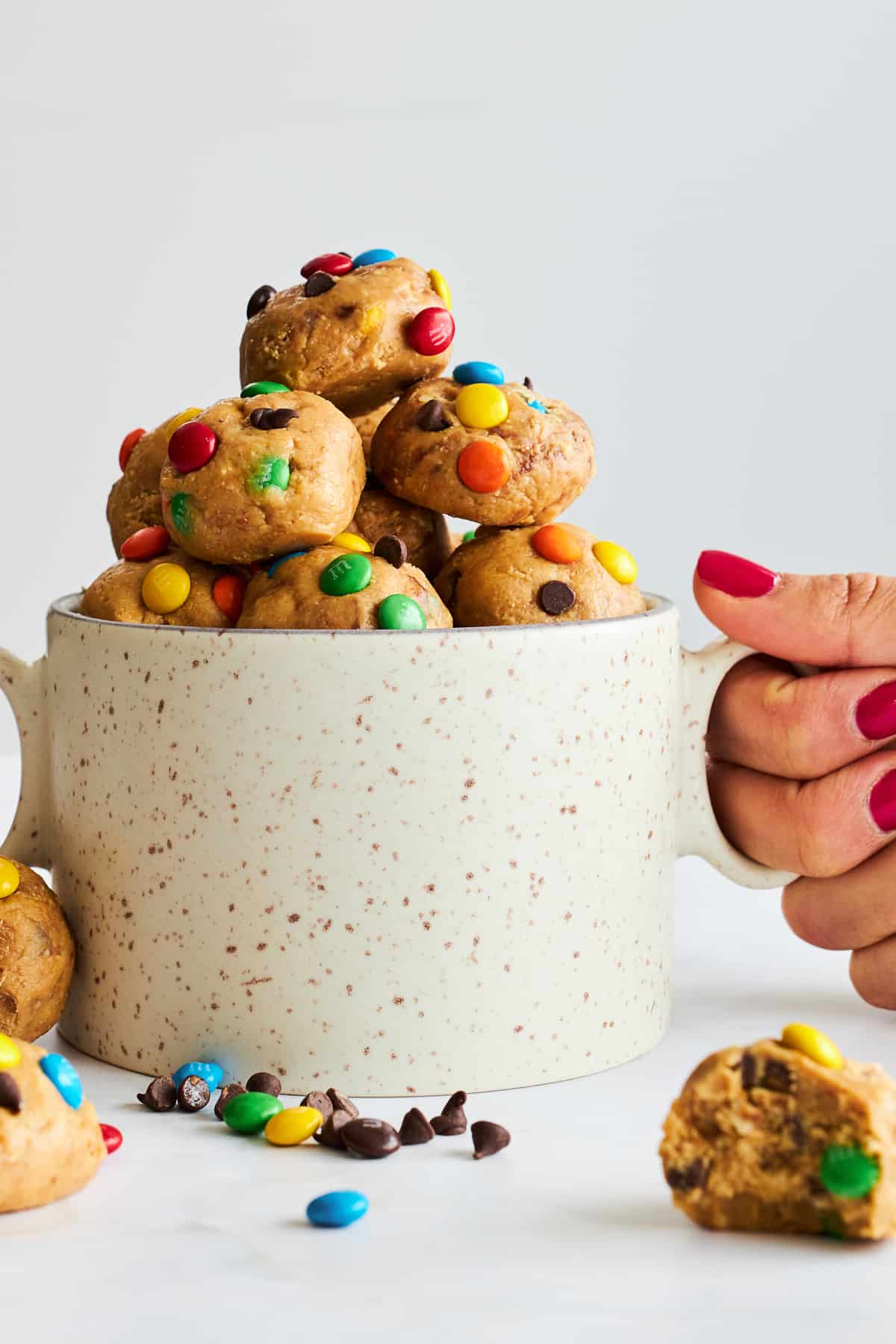 A hand holding a mug full of monster cookie energy bites. 