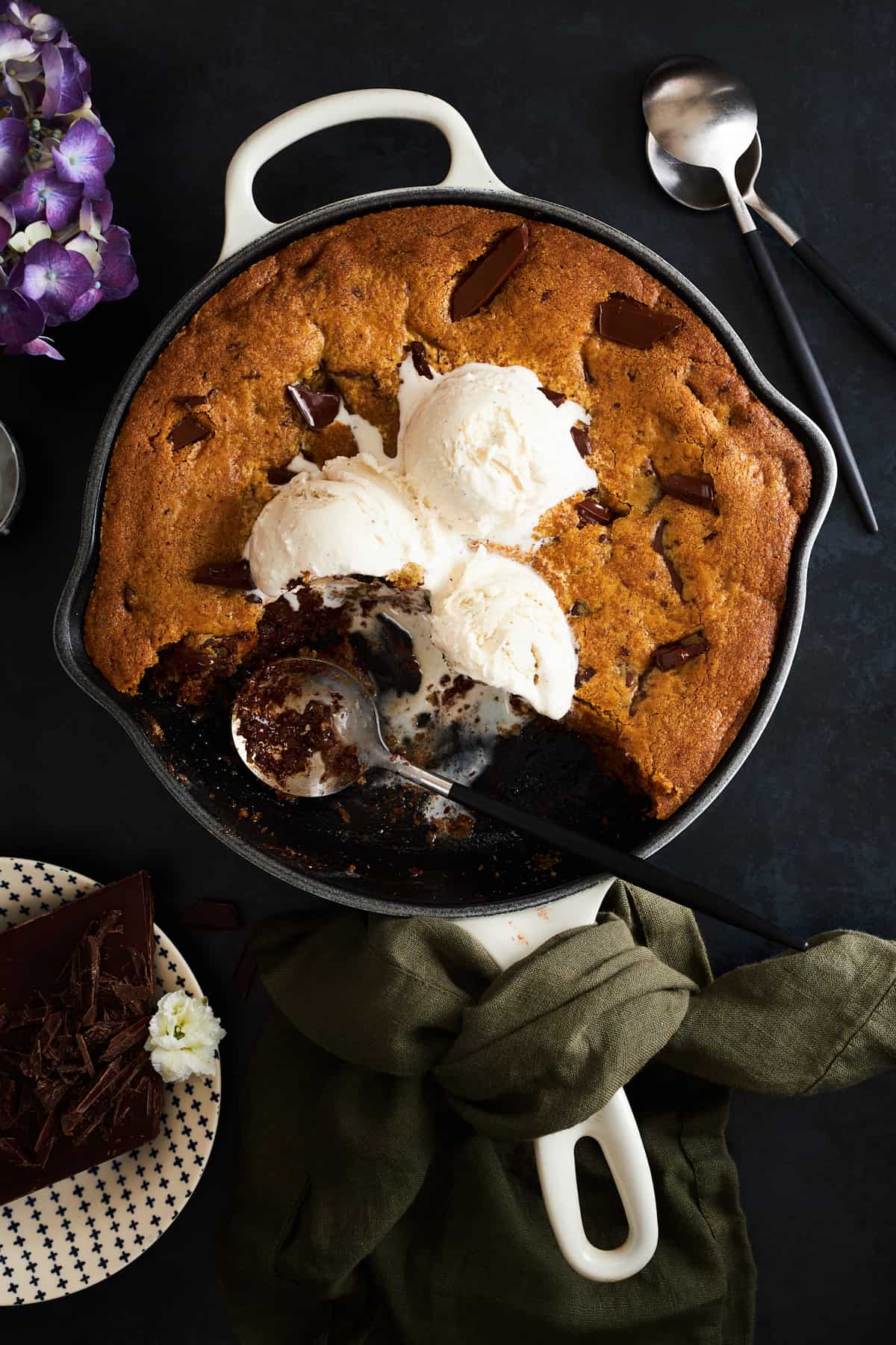 A skillet chocolate chip cookie topped with ice cream with bites missing. 