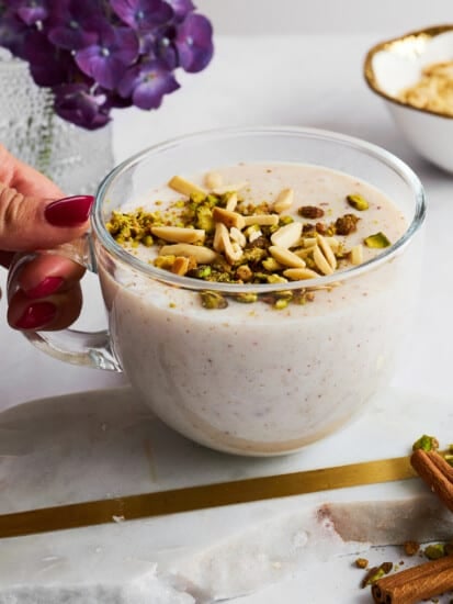A hand holding a mug of sahlab topped with crushed nuts.
